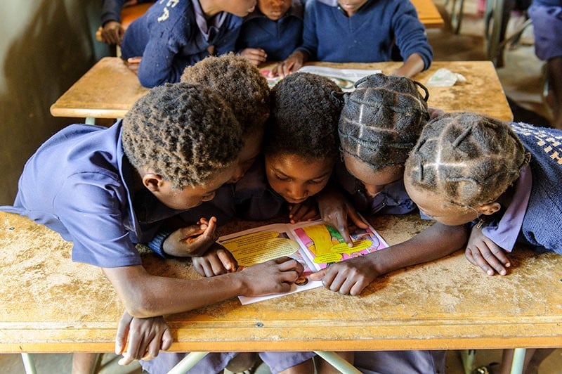 Five desk mates share a book during a reading lesson in class.